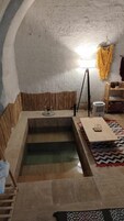 Una habitación con una bañera de piedra, una mesa de madera y una lámpara.