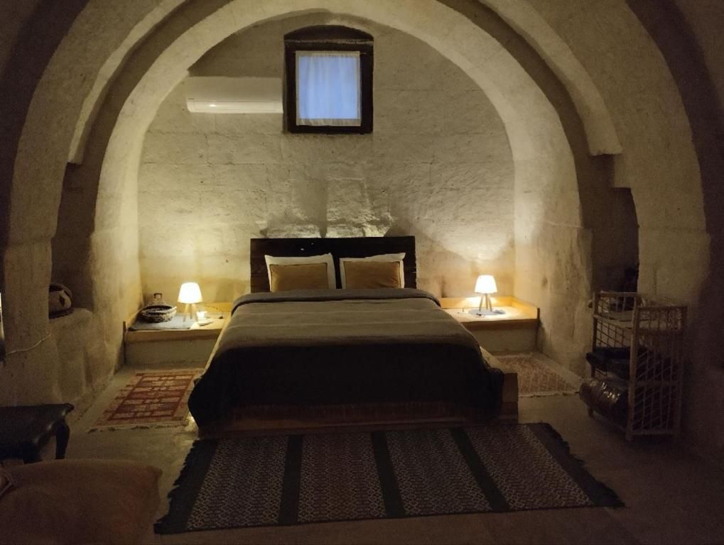 Ein Schlafzimmer mit gewölbter Decke, einem Bett mit Kopfteil, zwei Nachttischen mit Lampen und einem kleinen Fenster.