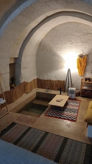 Um quarto com teto abobadado, área de estar central com mesa e cadeiras, e um tapete pequeno no chão.