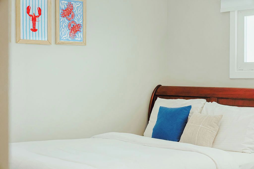 Un dormitorio con cabecera de madera, ropa de cama blanca y dos cuadros en la pared.