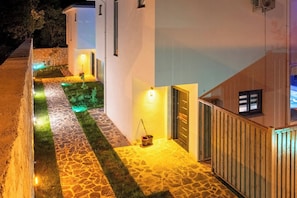 A pathway leading to a building with a stone-tiled entrance and a small garden area with artificial grass. - Villa Savaya-2 Antalya (Kaş)