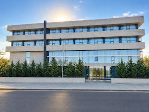 A modern building with a flat roof, multiple windows, and a paved entrance area.