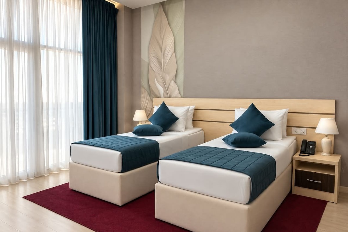 Habitación de hotel con dos camas, una alfombra roja, cabecero de madera y una pared con diseño de hojas.