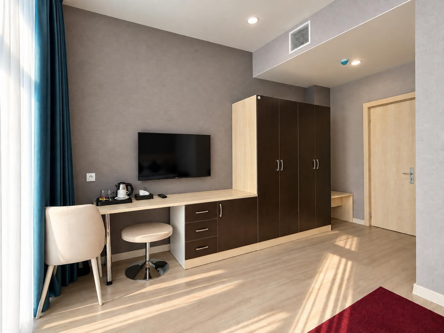 Ein modernes Zimmer mit Schreibtisch, Stuhl, Fernseher, Kleiderschrank und einem roten Teppich.