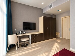 A modern room with a desk, chair, television, wardrobe, and a red rug.