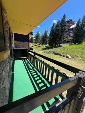 Ein Balkon mit grünem Boden, einem gelben Sonnensegel und einer Steinmauer.