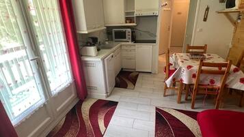 Une cuisine compacte équipée d’un four à micro-ondes, d’un grille-pain et d’un évier. On y trouve également un coin repas avec une table et des chaises, ainsi qu’un canapé rouge.