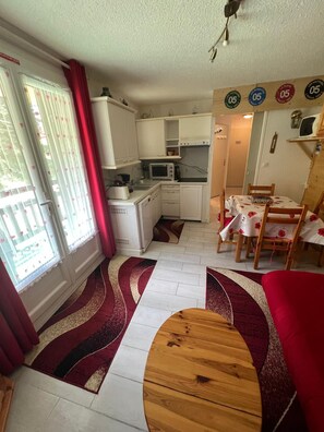 Eine kompakte Küche mit Mikrowelle, Toaster und Spüle. Ein Essbereich mit Tisch und Stühlen sowie ein rotes Sofa vorhanden.