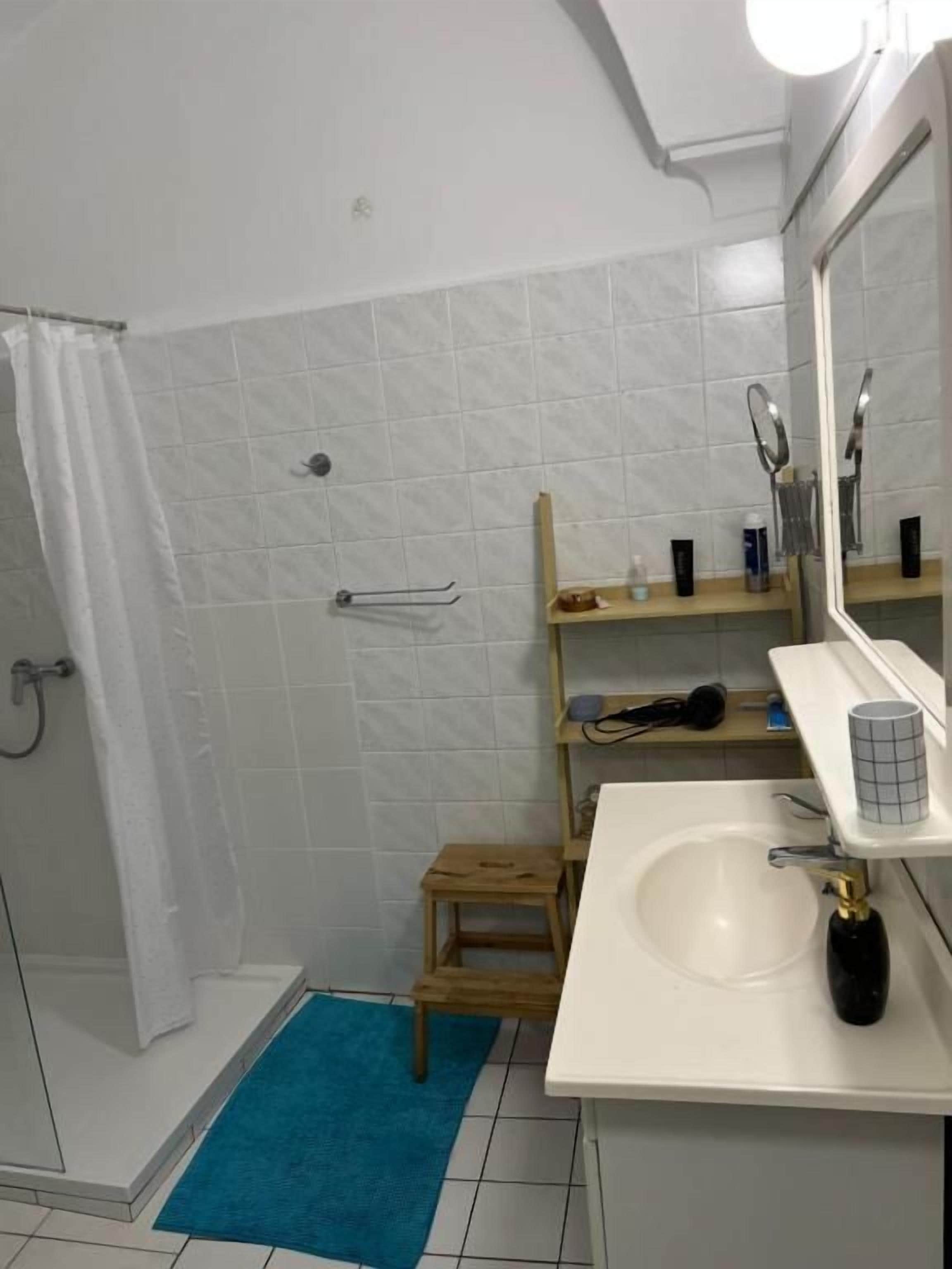 A bathroom with a shower, a sink, a mirror, and a small wooden stool.