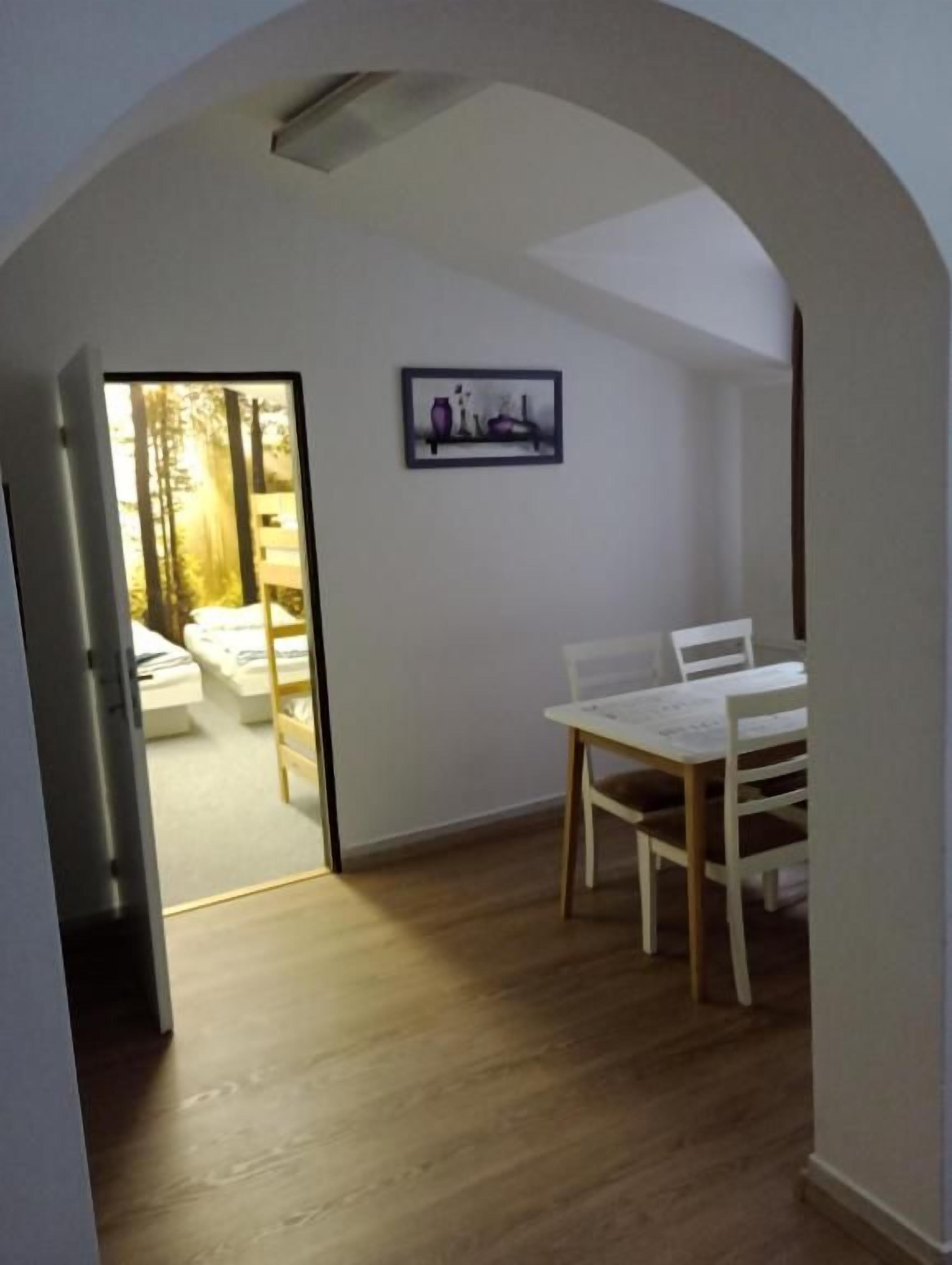 Una habitació amb taula i cadires, un quadre encadrado a la paret, i una porta d'arc que condueix a una altra habitació.
