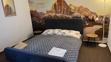 Una habitación de hotel con una cama, una lámpara de pared y un cuadro de un paisaje de montaña.