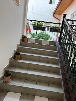 A staircase with a metal railing, potted plants at the bottom, and a view of a building with a red awning in the background. - GRAN hostel (Banska Bystrica)