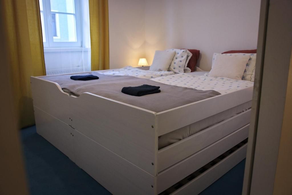 A single-bed room with a wooden frame, a window with yellow curtains, a bedside lamp, and a bed with a white and blue patterned bedspread.