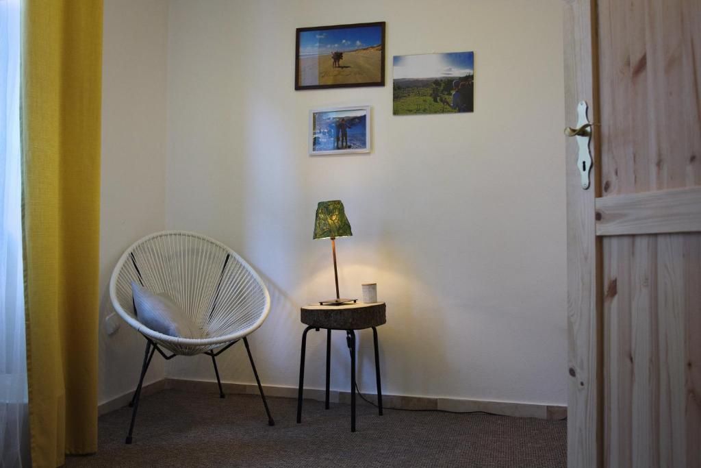 Una habitación con una silla blanca, una mesita con una lámpara y tres cuadros en la pared.