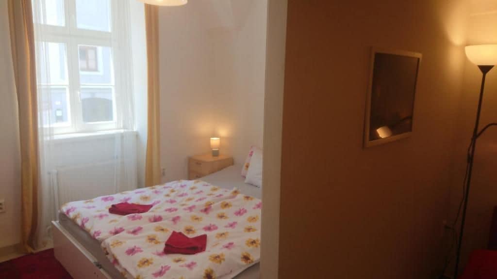 Habitación de hotel con cama, mesita de noche, lámpara y ventana con cortinas.