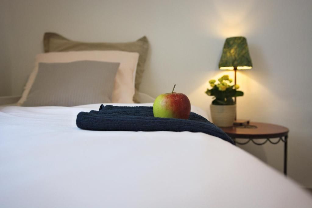 A bed with a single apple and a folded towel, a lamp, and a small table with flowers.
