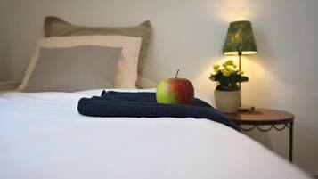 A bed with a single apple and a folded towel, a lamp, and a small table with flowers.