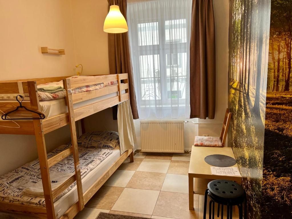 A room with bunk beds, a table, a chair, a hanging lamp, and a window with curtains.