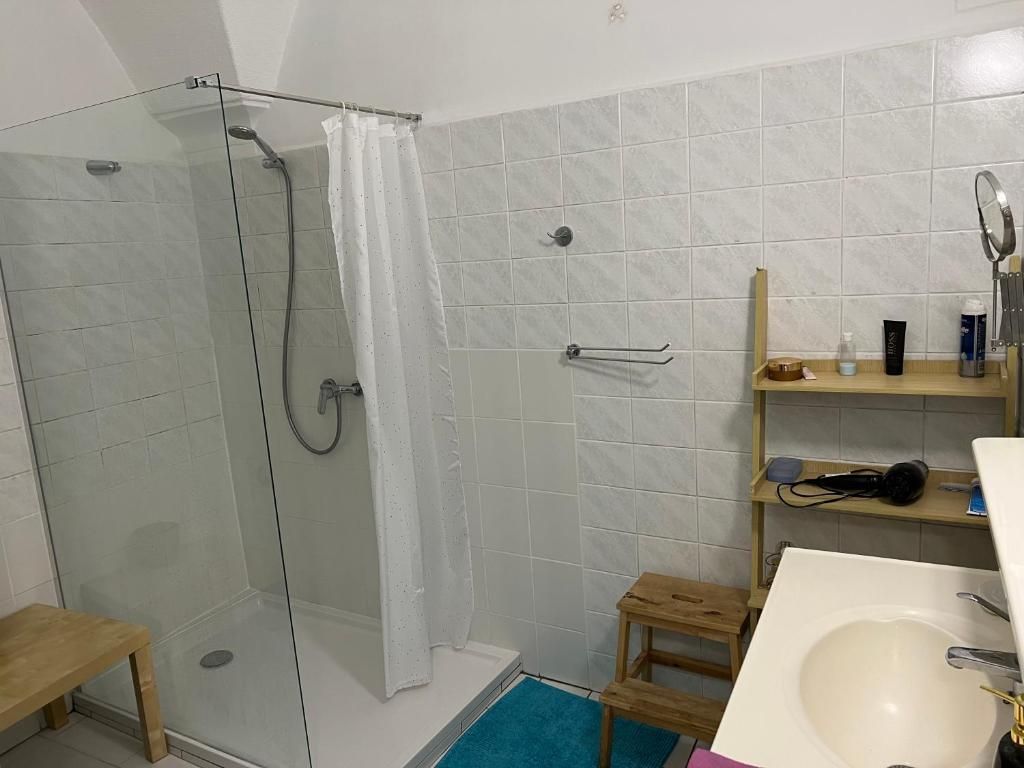 Un baño con ducha envuelta en vidrio, un lavamanos blanco y un banco de madera.
