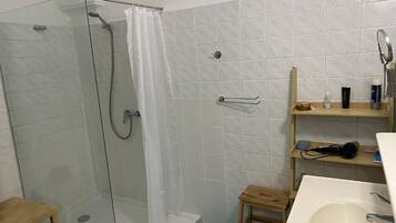 Un baño con ducha envuelta en vidrio, un lavamanos blanco y un banco de madera.