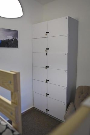 A white storage unit with multiple compartments, a framed picture on the wall, and a chair in the corner. - GRAN hostel (Banska Bystrica)