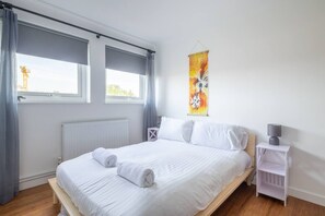 A bedroom with a bed, a nightstand, a window with curtains, and a wall-mounted artwork. - Chic 2bed ground floor flat with garden & parking (Cambridgeshire)