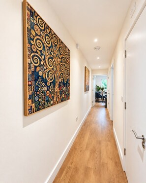 A hallway with a large abstract painting on the left wall, a wooden floor, and a door on the right. - Chic 2bed ground floor flat with garden & parking (Cambridgeshire)