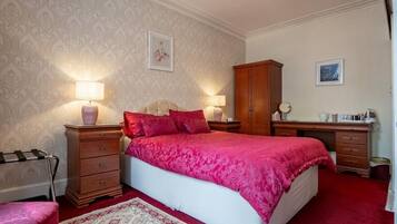 Un dormitorio con una cama grande, dos mesitas de noche, un armario de madera y una alfombra estampada.