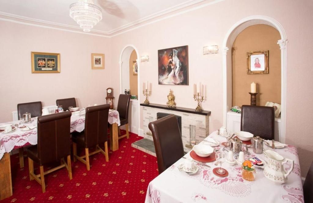 Comedor con alfombra roja, manteles blancos y sillas marrones. Se observan cuadros en las paredes y un candelabro sobre la mesa.