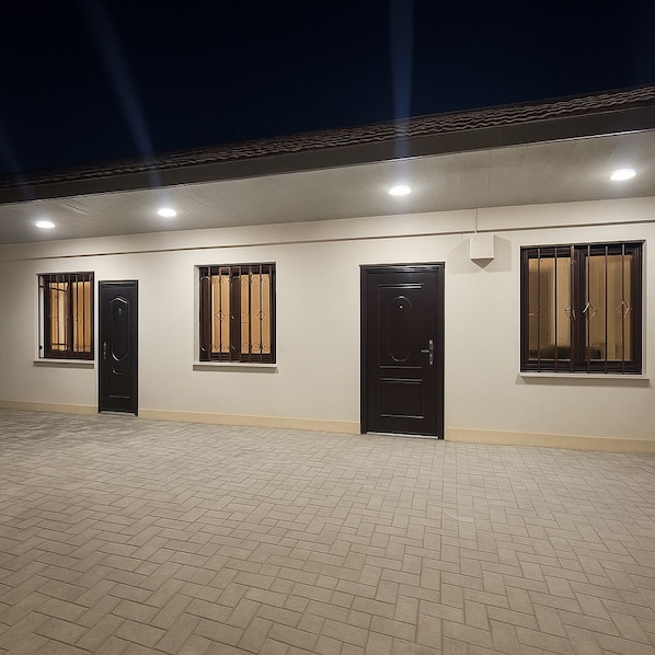 A building facade with three doors and windows, each with metal bars, under artificial lighting.