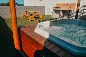A hot tub with a wooden deck, a brick wall, and a small outdoor table. - Morro Apartaments (Morro de São Paulo)