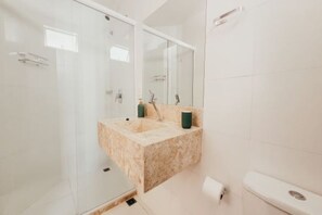A modern bathroom with a glass shower enclosure, a marble sink, and a large mirror. - Morro Apartaments (Morro de São Paulo)