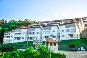 A multi-story residential building with balconies, a small garden area, and a visible street sign. - Morro Apartaments (Morro de São Paulo)