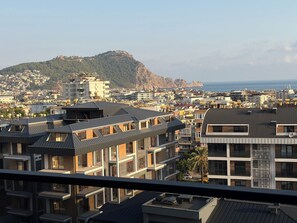A residential area with modern buildings, a mountain in the background, and a view of the sea. - Spacious 3-bedroom apartment in lovely Alanya with AC and gym access (Alanya)