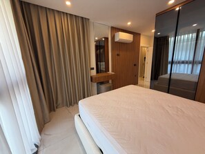 A modern hotel room with a large bed, a wooden panel wall, a mirror, and a window with curtains. - Spacious 3-bedroom apartment in lovely Alanya with AC and gym access (Alanya)