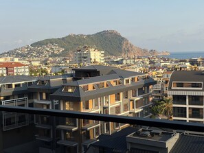 A modern residential area with multi-story buildings, flat roofs, and a view of a hill with a fort-like structure. - Spacious 3-bedroom apartment in lovely Alanya with AC and gym access (Alanya)