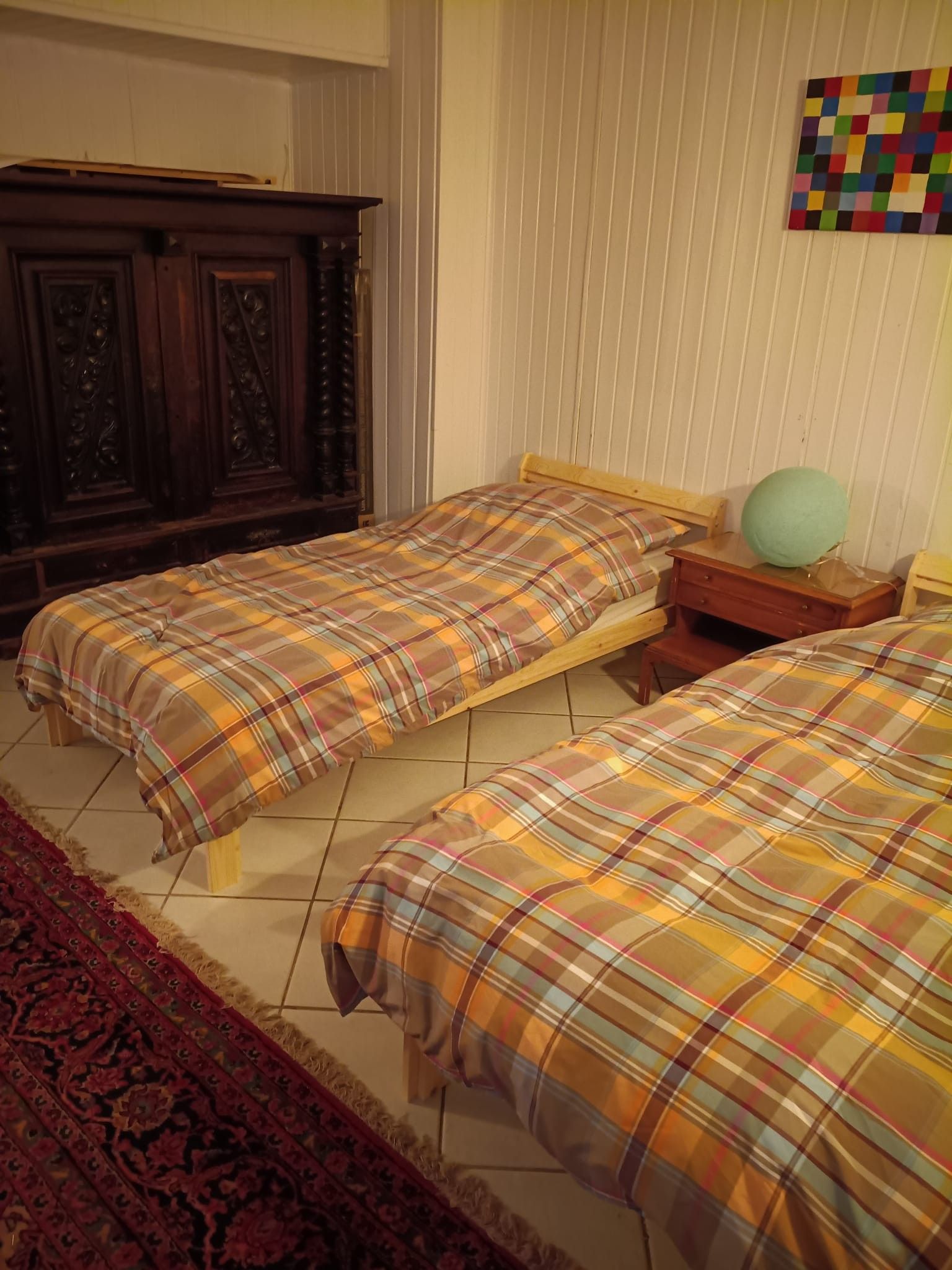 Un dormitorio con dos camas, un armario de madera, una mesita de noche pequeña y un tapiz de pared colorido.