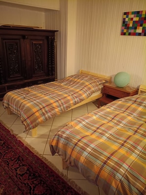 Un dormitorio con dos camas, un armario de madera, una mesita de noche pequeña y un tapiz de pared colorido.