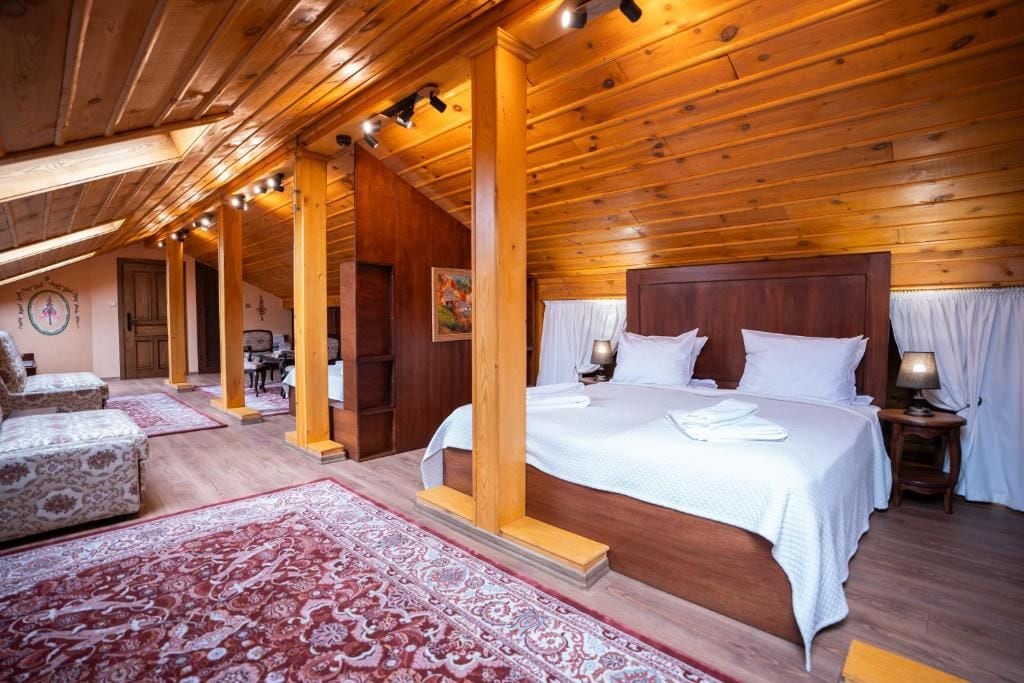 Un dormitorio estilo cabaña de madera con una cama grande, una zona de estar con sofá y una mesa de comedor.