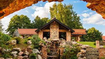 Un bâtiment en pierre surmonté d’un toit de tuiles rouges, entouré d’un jardin aménagé avec des rochers et une cascade.