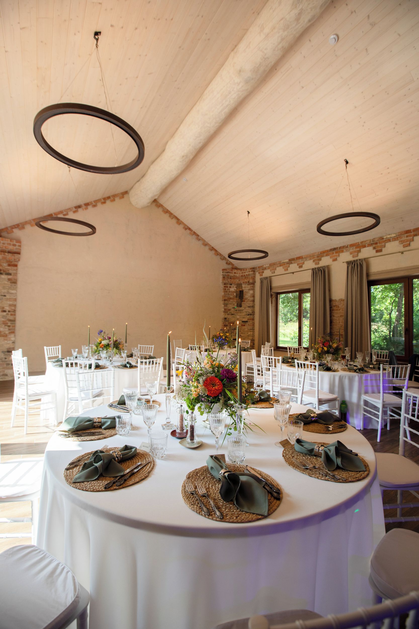 A dining area with round tables set for a meal, featuring woven placemats, cutlery, and floral centerpieces.