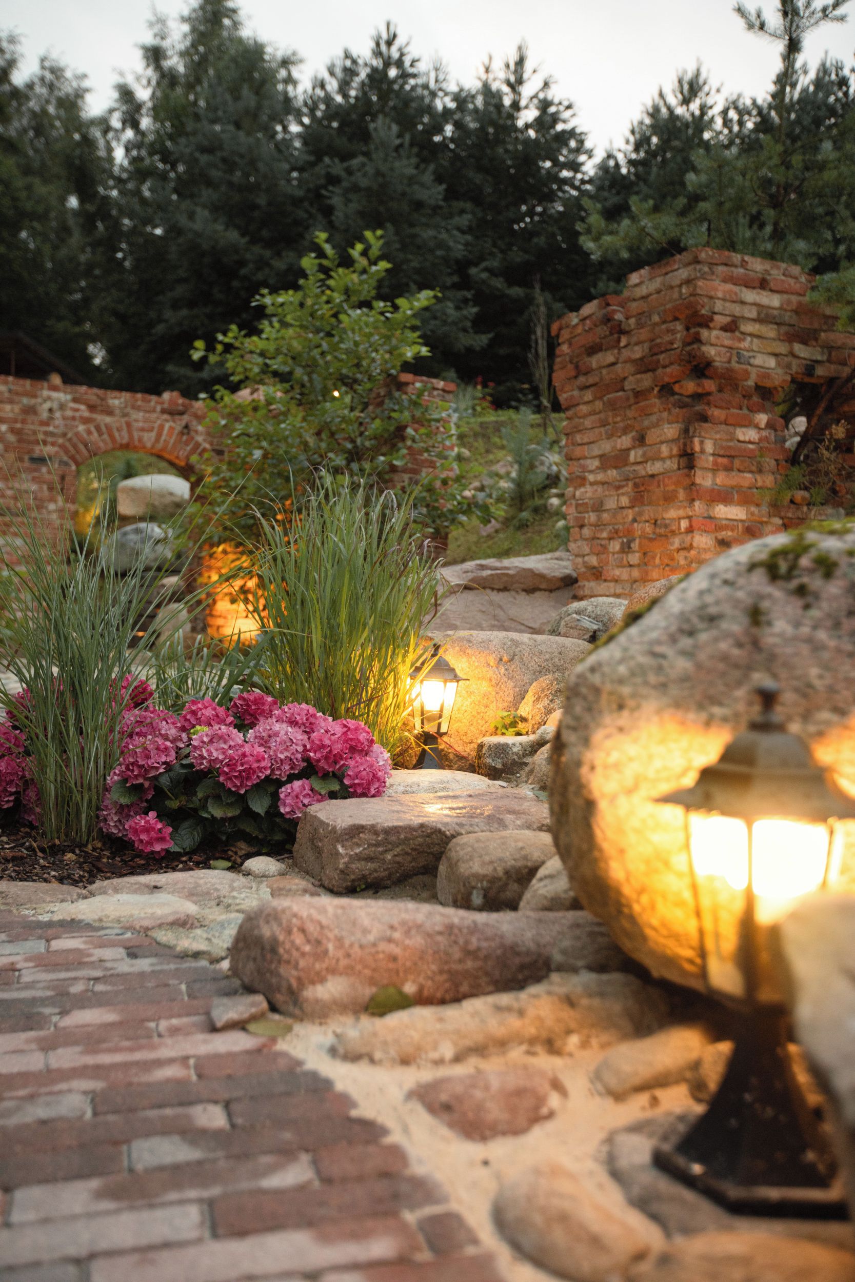A garden pathway with a brick wall, a stone lantern, and pink hydrangea bushes.