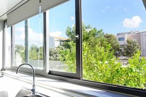 A modern kitchen with a window overlooking a green landscape and buildings. - Urban Living Home | Cozy Retreat (Agios Onoufrios)