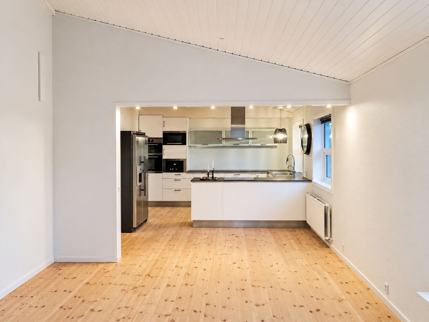 A modern kitchen with white cabinetry, stainless steel appliances, and a wooden floor.