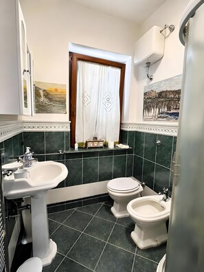 A bathroom with a pedestal sink, two toilets, a window with a curtain, and a painting on the wall. - Guest House 'Un Sogno - Bacco Suite' with Private Terrace, Shared Garden and Wi-Fi (Bassano Romano)