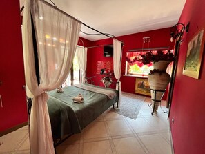 A room with a bed, a window with red curtains, a vase with flowers, and a painting on the wall. - Guest House 'Un Sogno - Bacco Suite' with Private Terrace, Shared Garden and Wi-Fi (Bassano Romano)