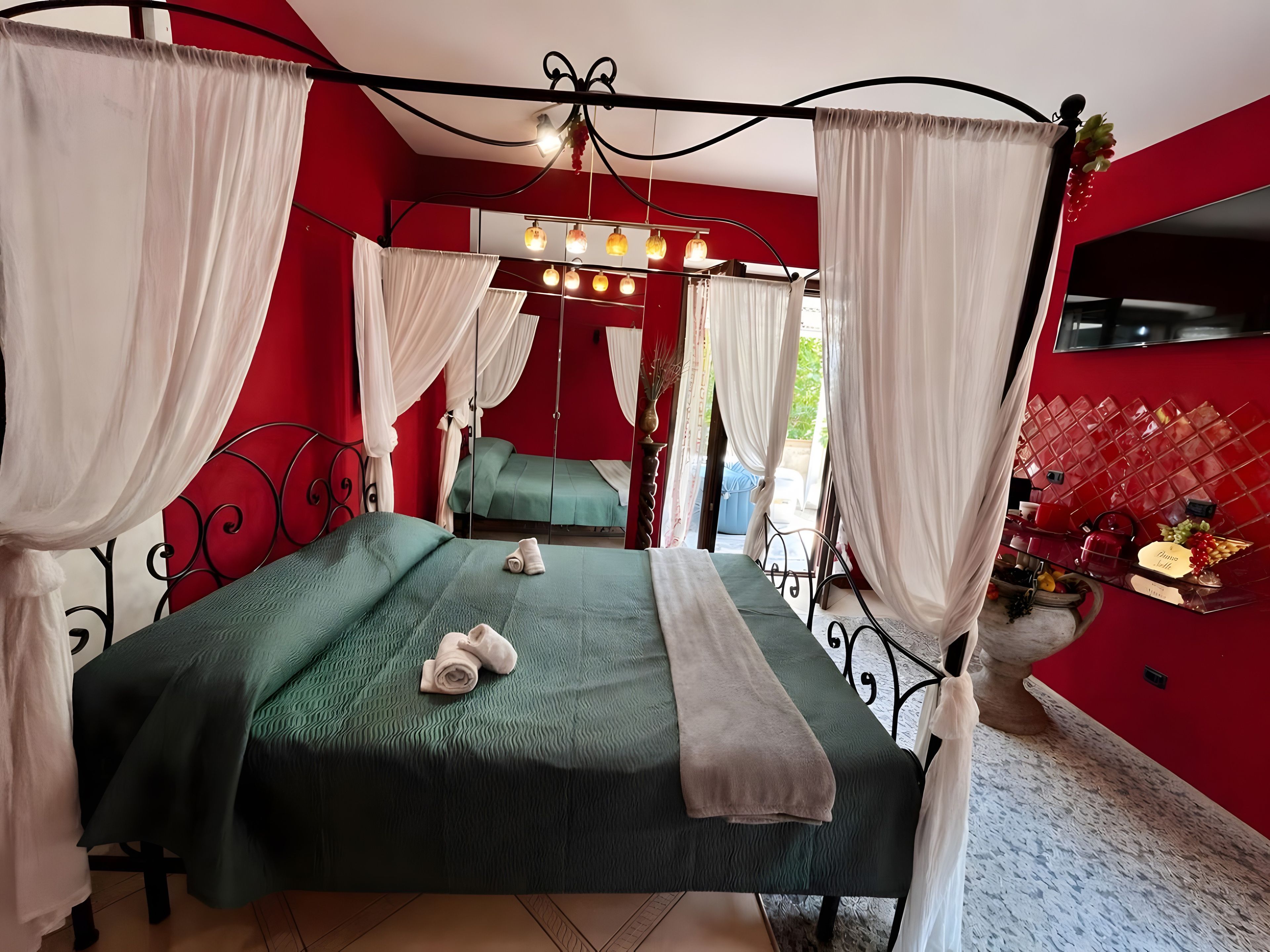 Une pièce avec un lit, un miroir et un mur rouge.