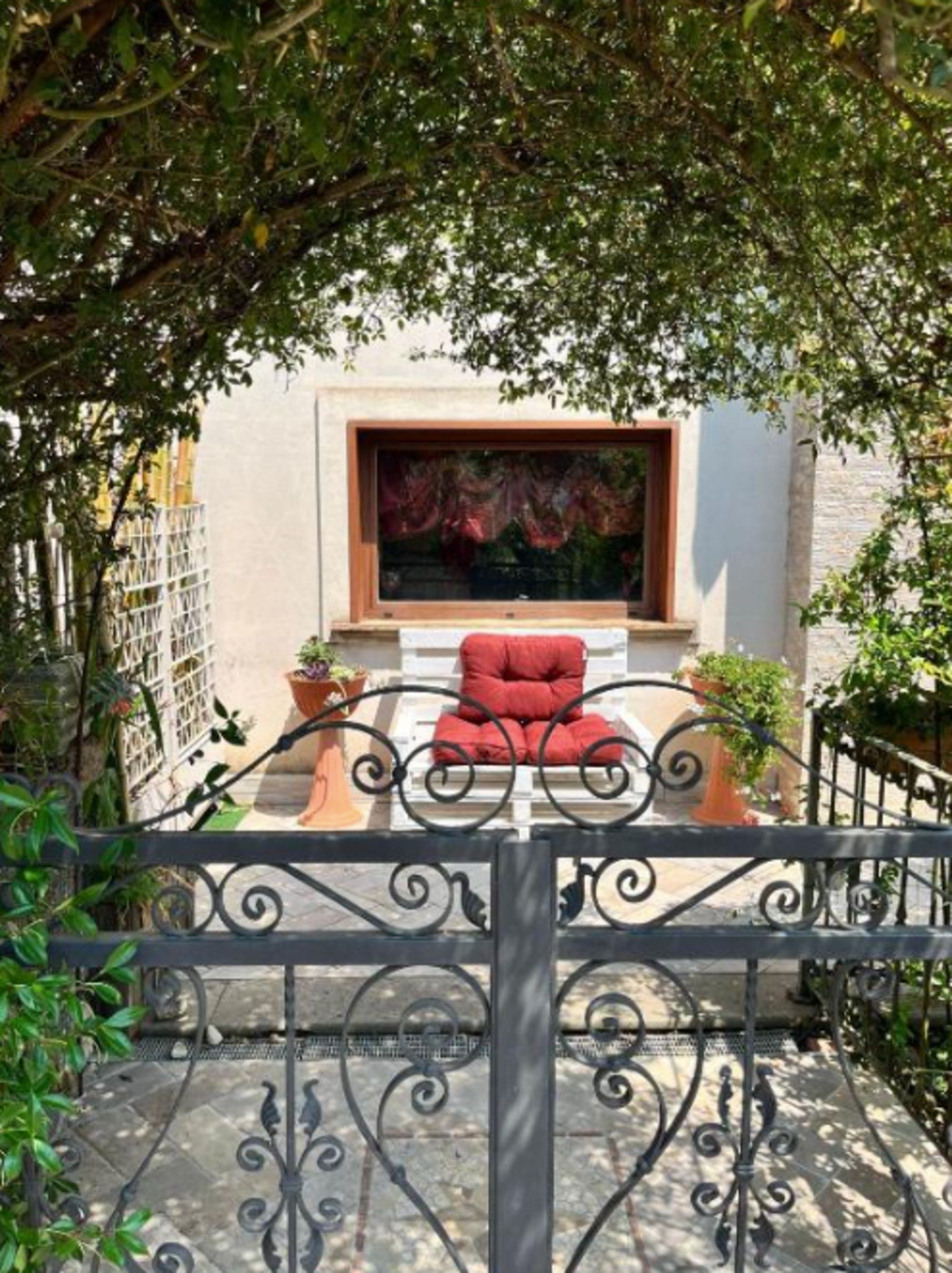 Une terrasse avec une chaise rouge, une plante en pot et une fenêtre ornée d’un tableau.