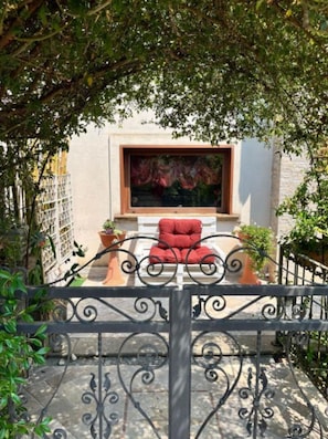Un patio con una silla roja, una planta en maceta y una ventana con un cuadro.