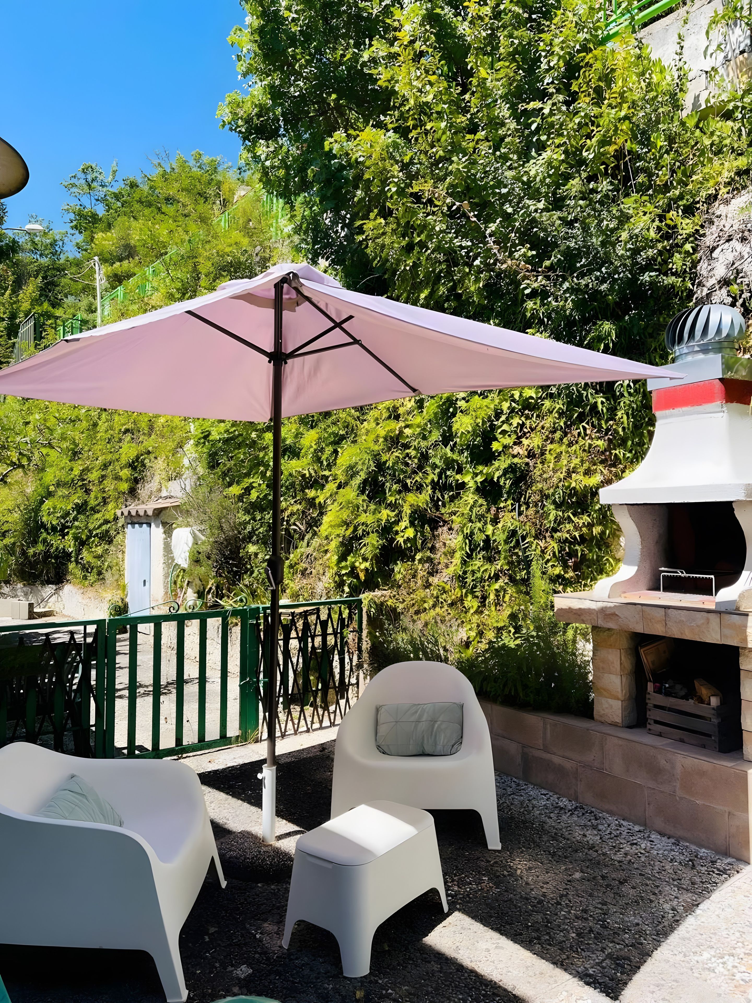 An outdoor seating area with a patio table, two chairs, a small stool, and a large umbrella.